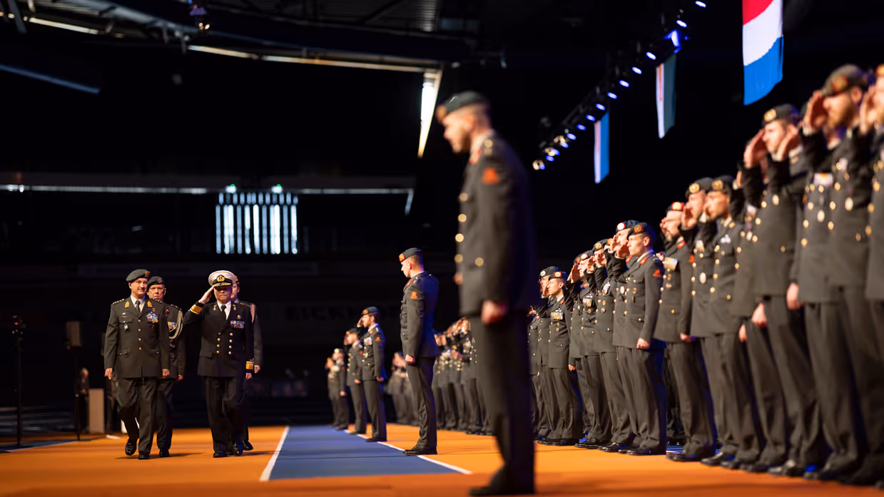 Parade-inspecteur loopt langs militairen tijdens medaille-uitreiking in sporthal.