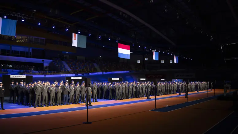 Militairen in dagelijks tenue staan naast elkaar opgesteld in een grote hal tijdens medaille-uitreiking.