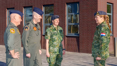 Luitenant-generaal André Steur, generaal-majoor Robert Adang en kolonel Martine Verhulst staan tegenover prinses Amalia buiten voor de Luchtmachttoren. Ze lachen naar elkaar en dragen allen operationele uniformen.