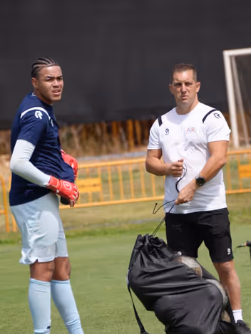 Een keeper met keepershandschoenen aan en een trainer met de ballentas. 