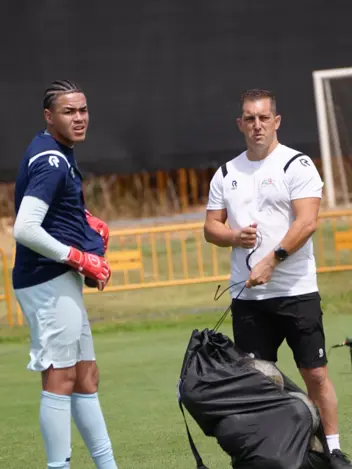 Een keeper met keepershandschoenen aan en een trainer met de ballentas. 