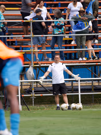 Een keeperstrainer staat op trainingsveld met gespreide armen achter een viertal ballen. 