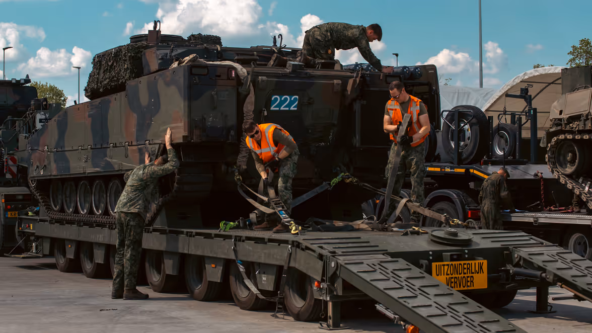 Militairen zetten een pantservoertuig vast op een vrachtwagen. 