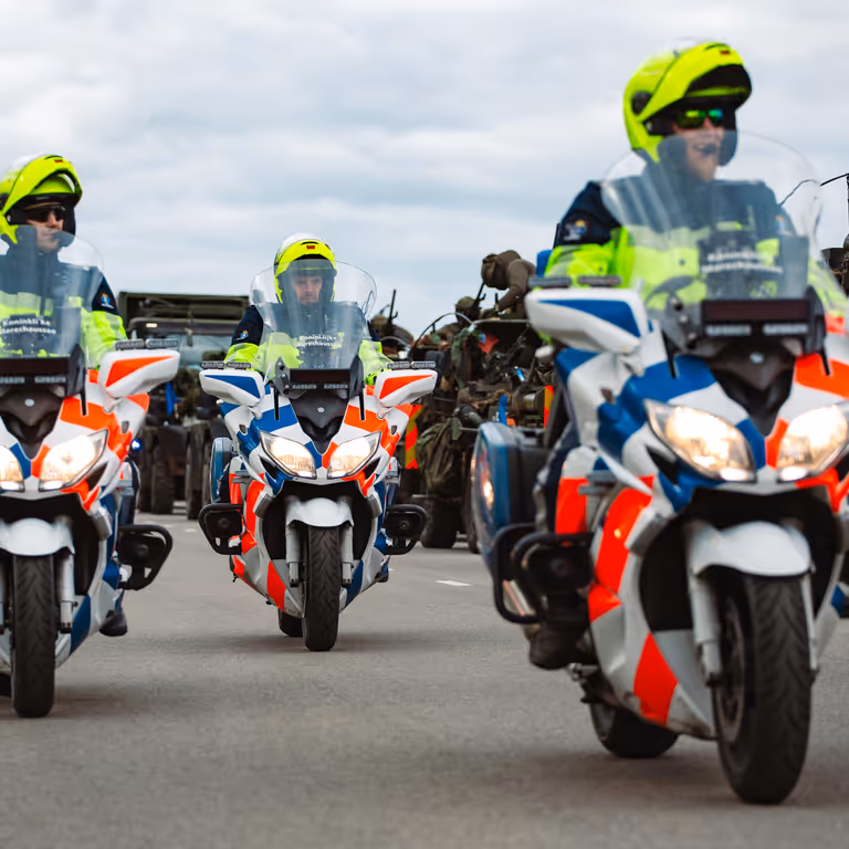 Motoren marechaussee rijden naast militaire voertuigen.