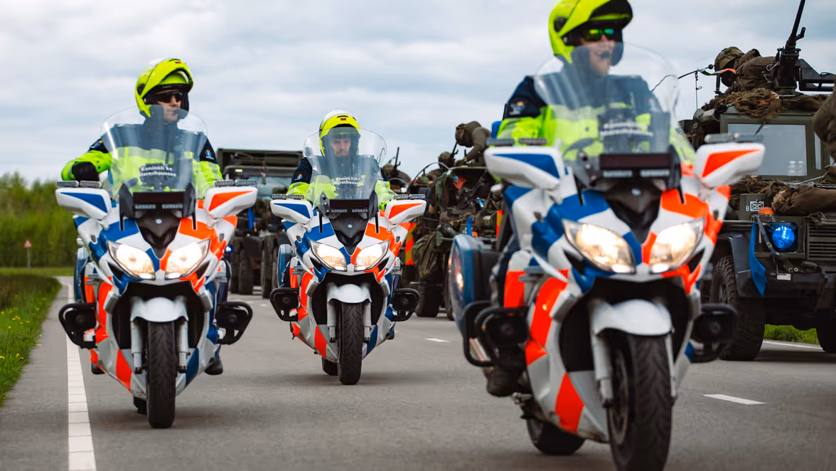 Motoren marechaussee rijden naast militaire voertuigen.