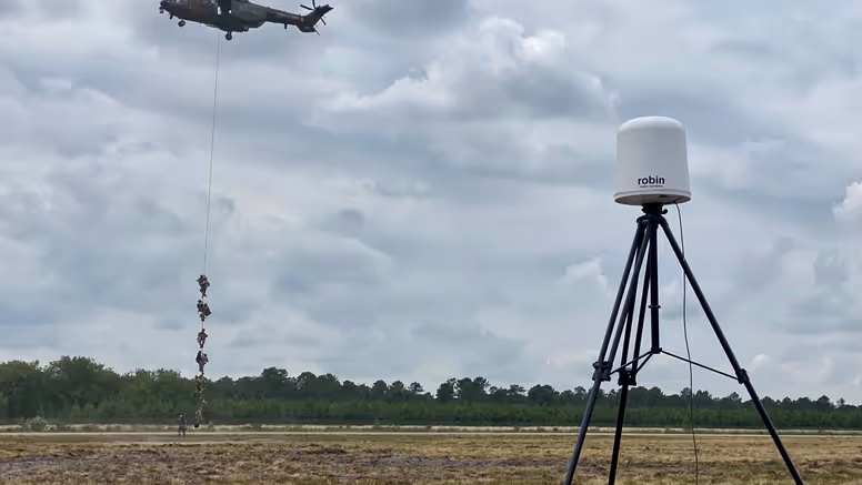 Op de voorgrond een radar, op de achtergrond militairen die met een touw afdalen uit een helikopter. 