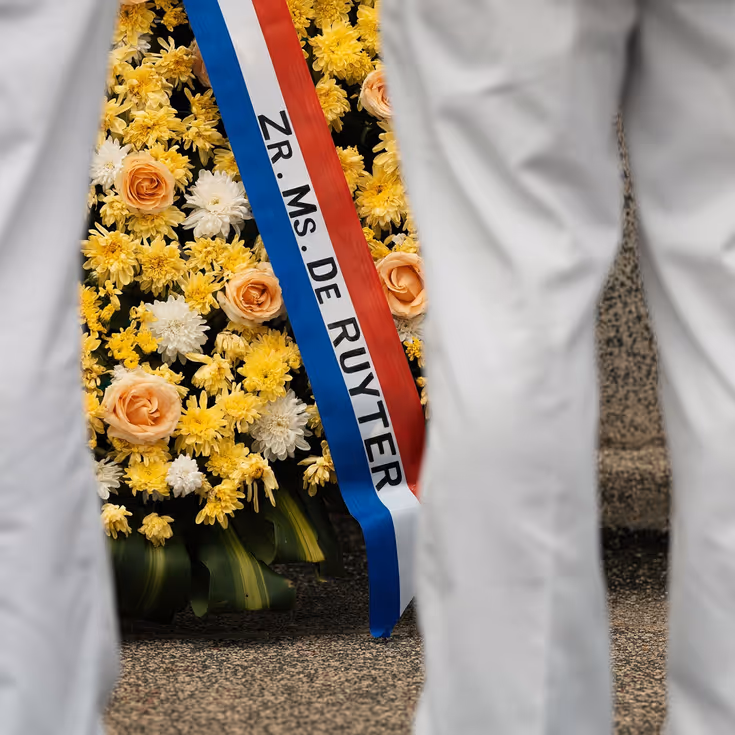 Militairen staan in tropentenue opgesteld op een militair ereveld in Soerabaja, op Java, en brengen de militaire groet. Op de andere foto staat de krans met opdruk Zr.Ms. De Ruyter die zij net hebben gelegd.  &nbsp;