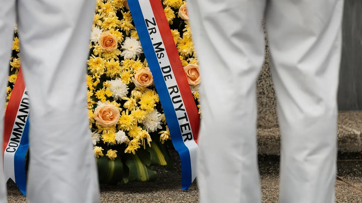Militairen staan in tropentenue opgesteld op een militair ereveld in Soerabaja, op Java, en brengen de militaire groet. Op de andere foto staat de krans met opdruk Zr.Ms. De Ruyter die zij net hebben gelegd.  &nbsp;