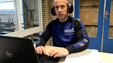 Jeroen Blomen met gehoorbescherming achter zijn laptop met een trui van Limburgse Waterleidingen aan. 