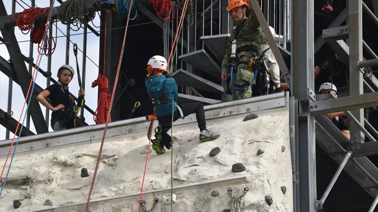 Kinderen abseilen terwijl een militair hen in de gaten houdt.