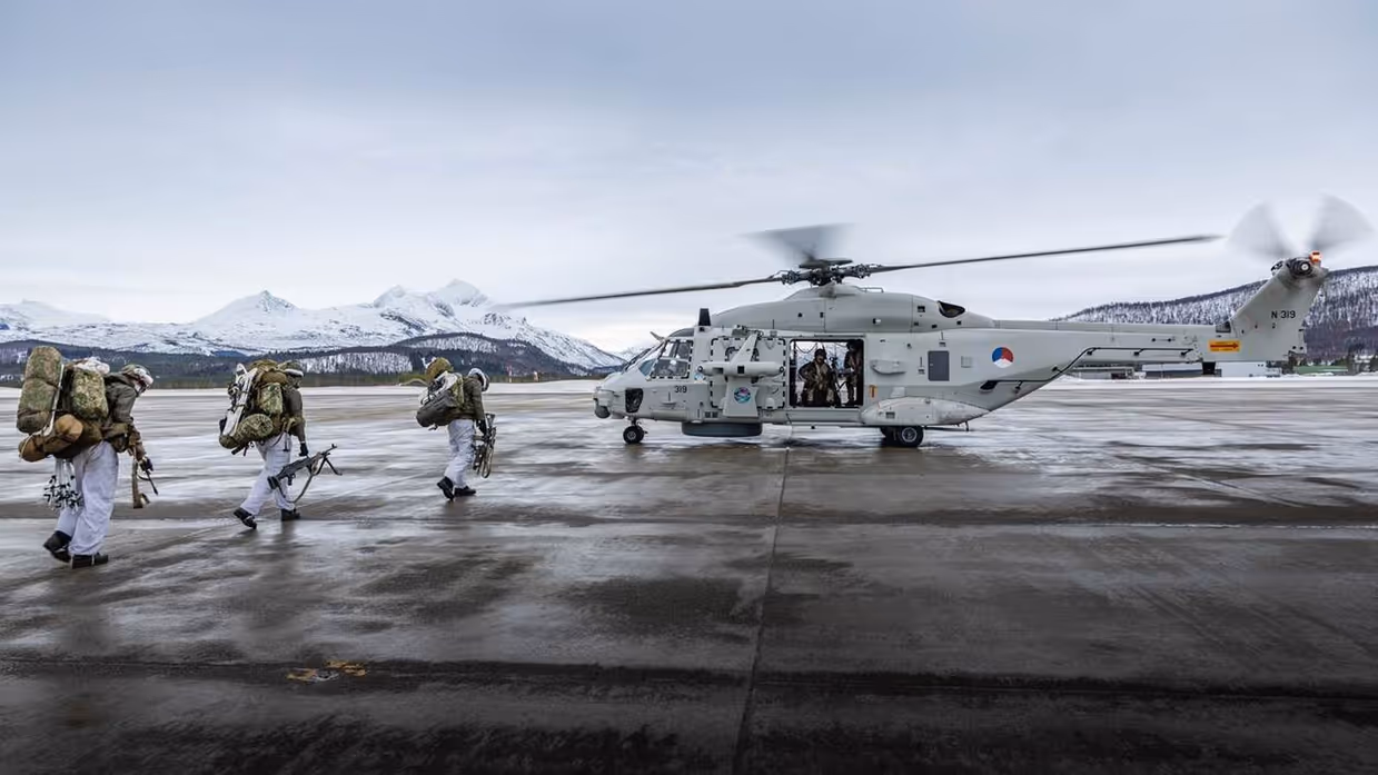 Militairen in witte kleding lopen naar NH-90 maritieme gevechtshelikopter aan boord van marineschip.