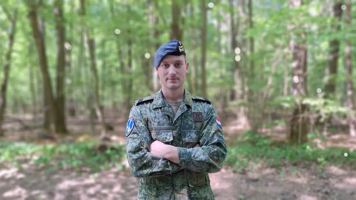 Sergeant Jorrin staat met armen over elkaar met een bos op de achtergrond. Foto: Defensie