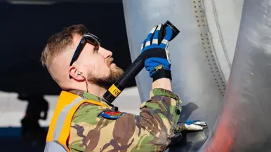 Technici staan onder de geopende motorgondel van een KDC-10 in een onderhoudshangar.