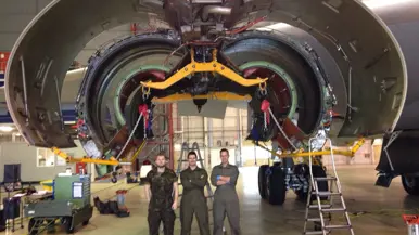 Technici staan onder de geopende motorgondel van een KDC-10 in een onderhoudshangar.