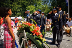Militairen van het Multicultureel Netwerk Defensie salueren bij het Nationaal Monument Slavernijverleden. Een krans met bloemen op de voorgrond.