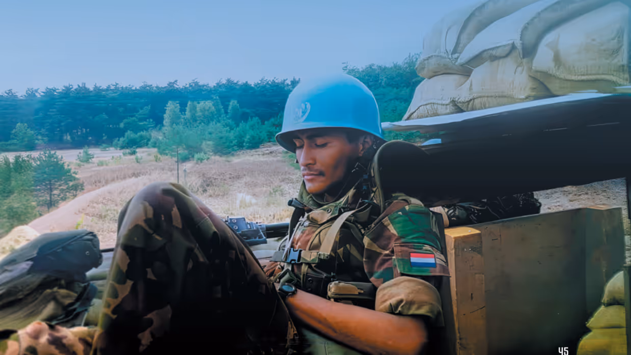 Een militair met een blauwe helm is iets aan het lezen op een berg, omgeven door zandzakken.