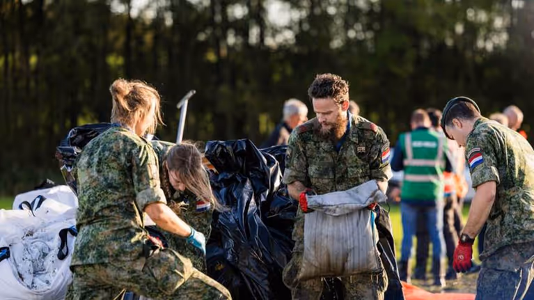 Mannelijke  en vrouwelijke militairen zijn bezig met zandzakken.