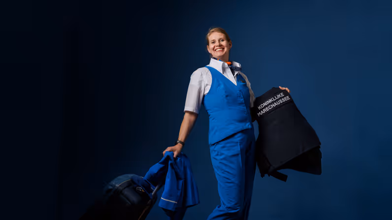 Portret van adjudant Elviera in KLM-pakje en met KMar-jas in de hand.