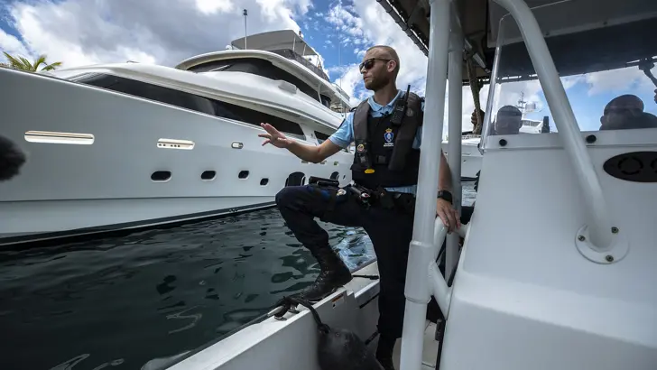 Een marechaussee staat op een boot en vaart langs een jacht.