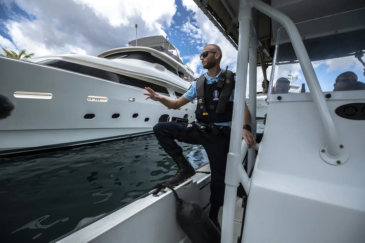 Een marechaussee staat op een boot en vaart langs een jacht.