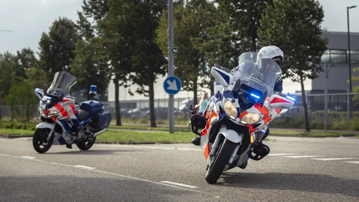 Een marechaussee rijdt op een motor de hoek om. 1 motor staat geparkeerd als wegafzetting.
