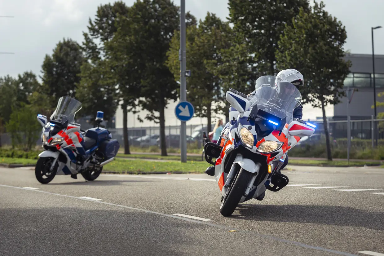 Een marechaussee rijdt op een motor de hoek om. 1 motor staat geparkeerd als wegafzetting.