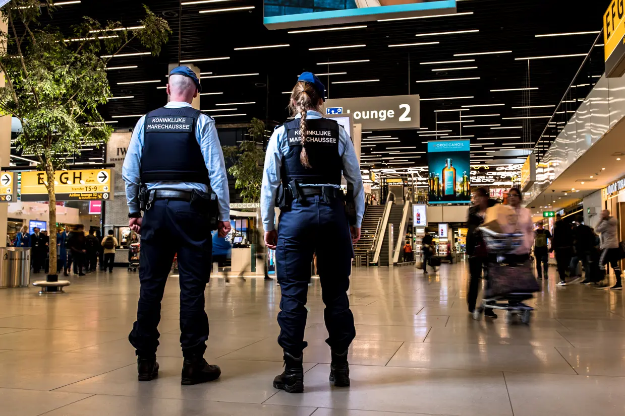 2 marechaussees op de rug gezien staan in een hal.