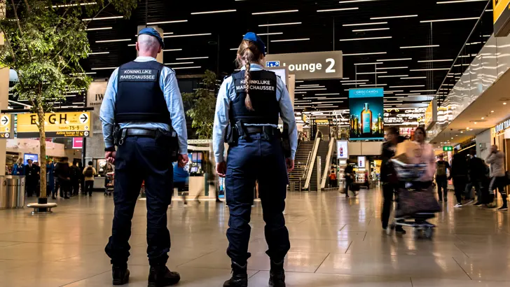 2 marechaussees op de rug gezien staan in een hal.