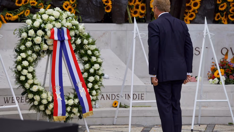 De koning staat voor de krans bij het monument. 