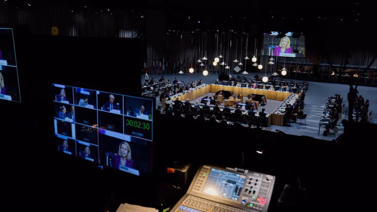 Grote vergadertafel met schermen op voorgrond. 