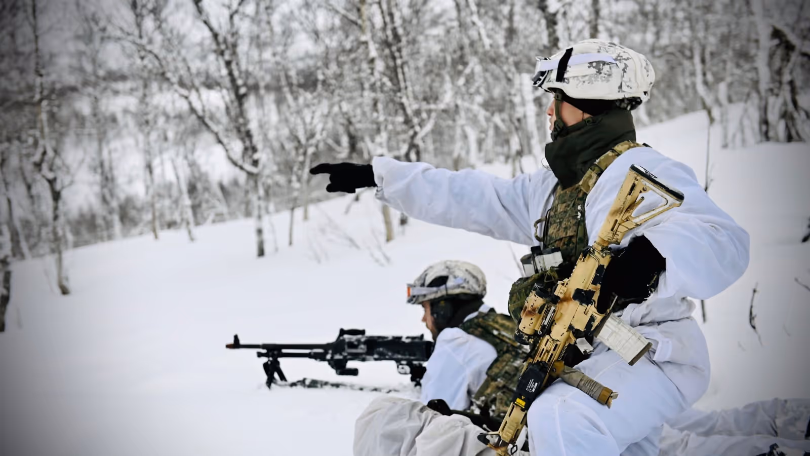 Twee militairen in witte kleding op patrouille in de sneeuw.