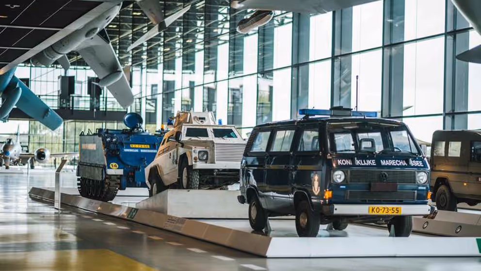 Voertuigen van de marechaussee op de museumvloer. Op de voorgrond een deel van een vliegtuig.
