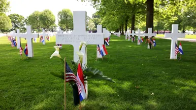 Een wit kruis met de tekst: Here rest in honored glory, a comrade in arms, known but to god. In de achtergrond nog meer kruisen, allemaal voorzien van een klein Amerikaans en Nederlands vlaggetje en een aantal is voorzien van bloemen.  