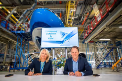 Vrouw en man achter tafel in vliegtuighangar ondertekenen samenwerkingsovereenkomst.