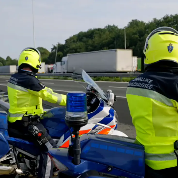 Twee motorrijders staan langs de snelweg en houden het verkeer in de gaten.