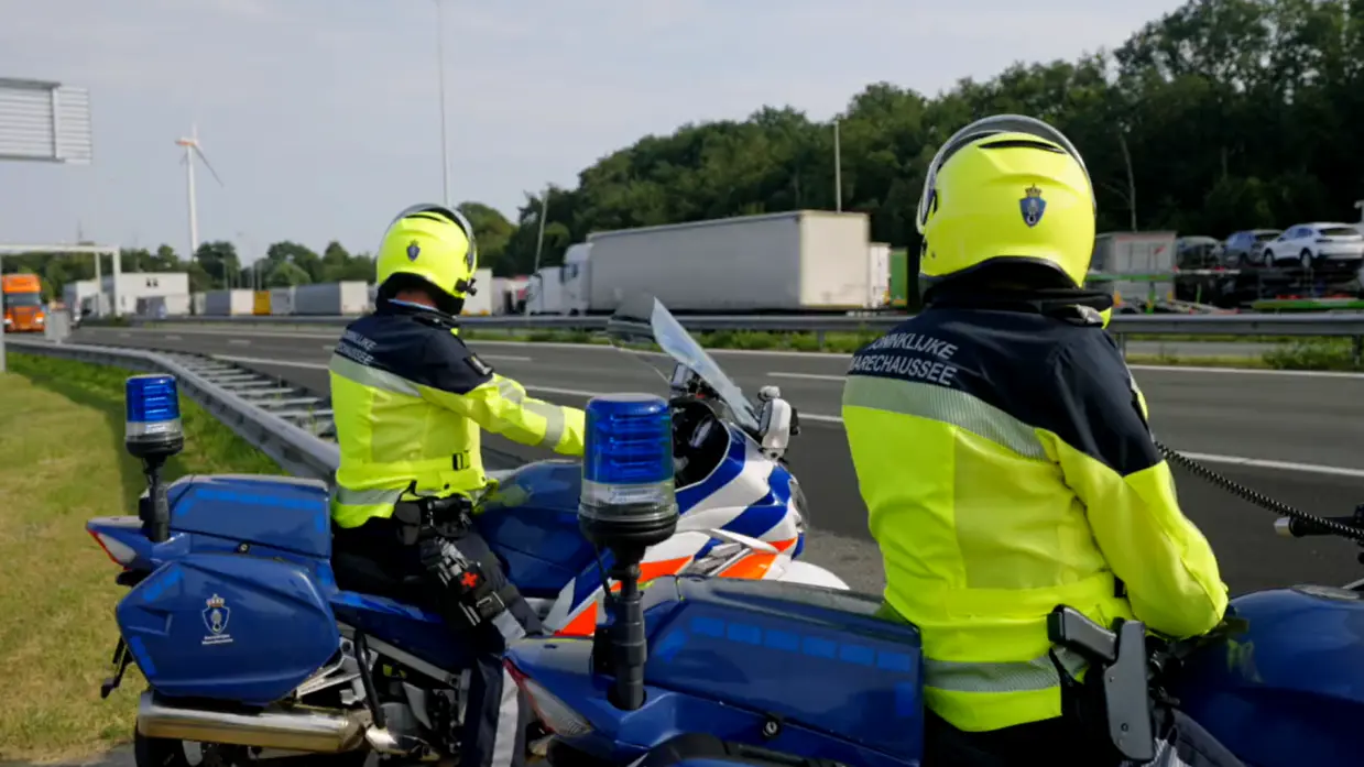 Twee motorrijders staan langs de snelweg en houden het verkeer in de gaten.
