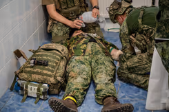 Gewonde militair ligt op zijn rug op de grond. Hij wordt behandeld.