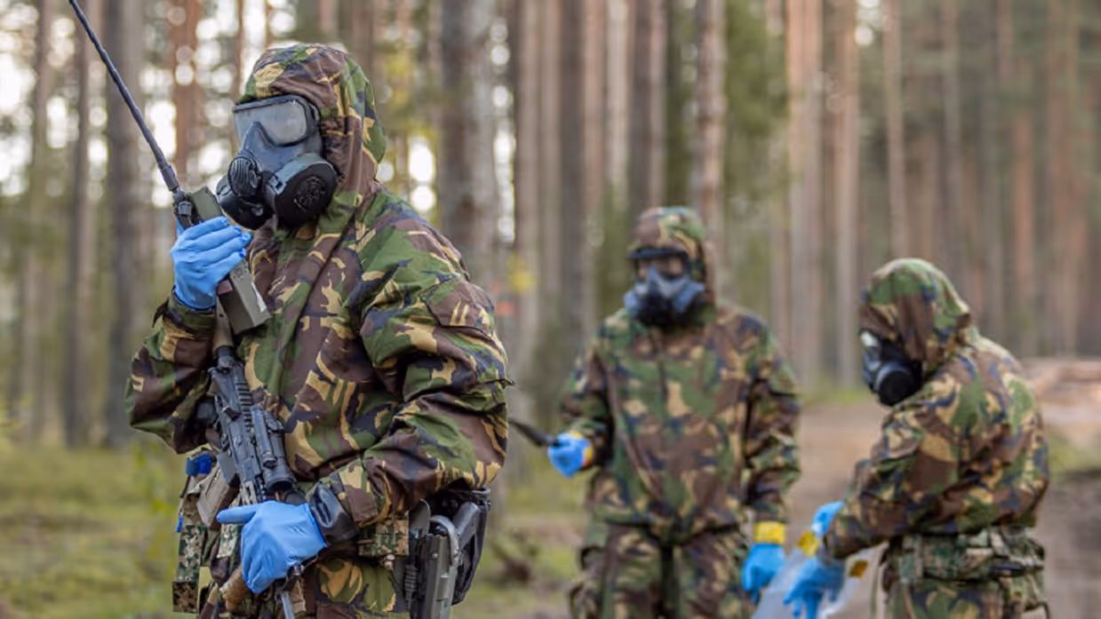 3 militairen met gasmaskers op in bos bij oefening in Litouwen.