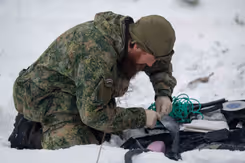 Militair op knieen in de sneeuw bezig met bevestiging van draden.