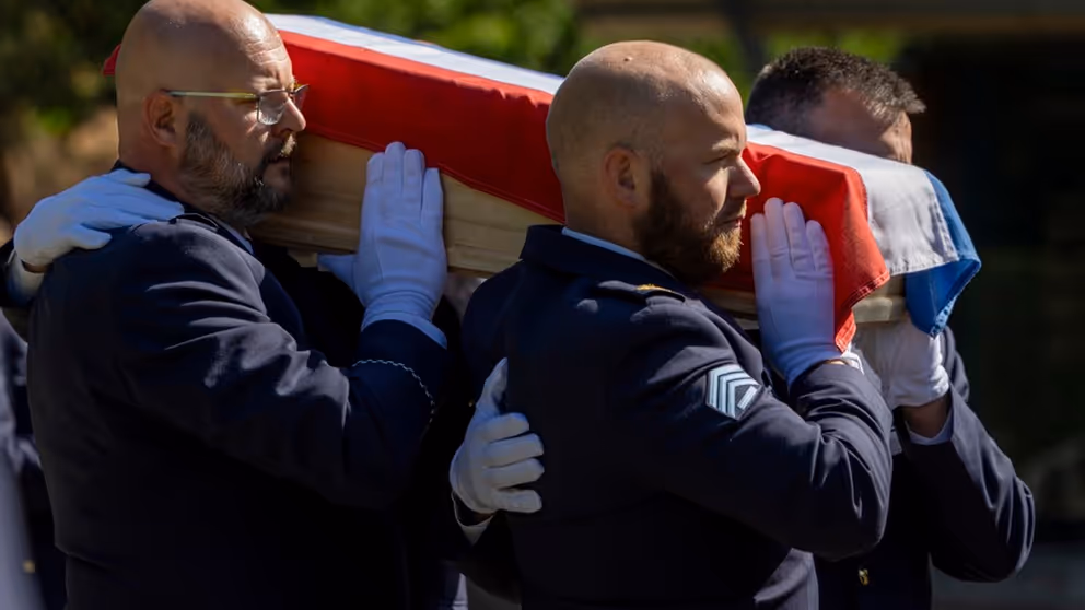Militairen dragen kist met Nederlandse vlag tijdens herbegrafenis.