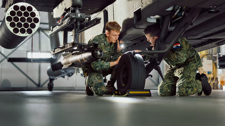Vliegtuigtechnici plegen onderhoud aan de onderkant van een gevechtshelikopter. 