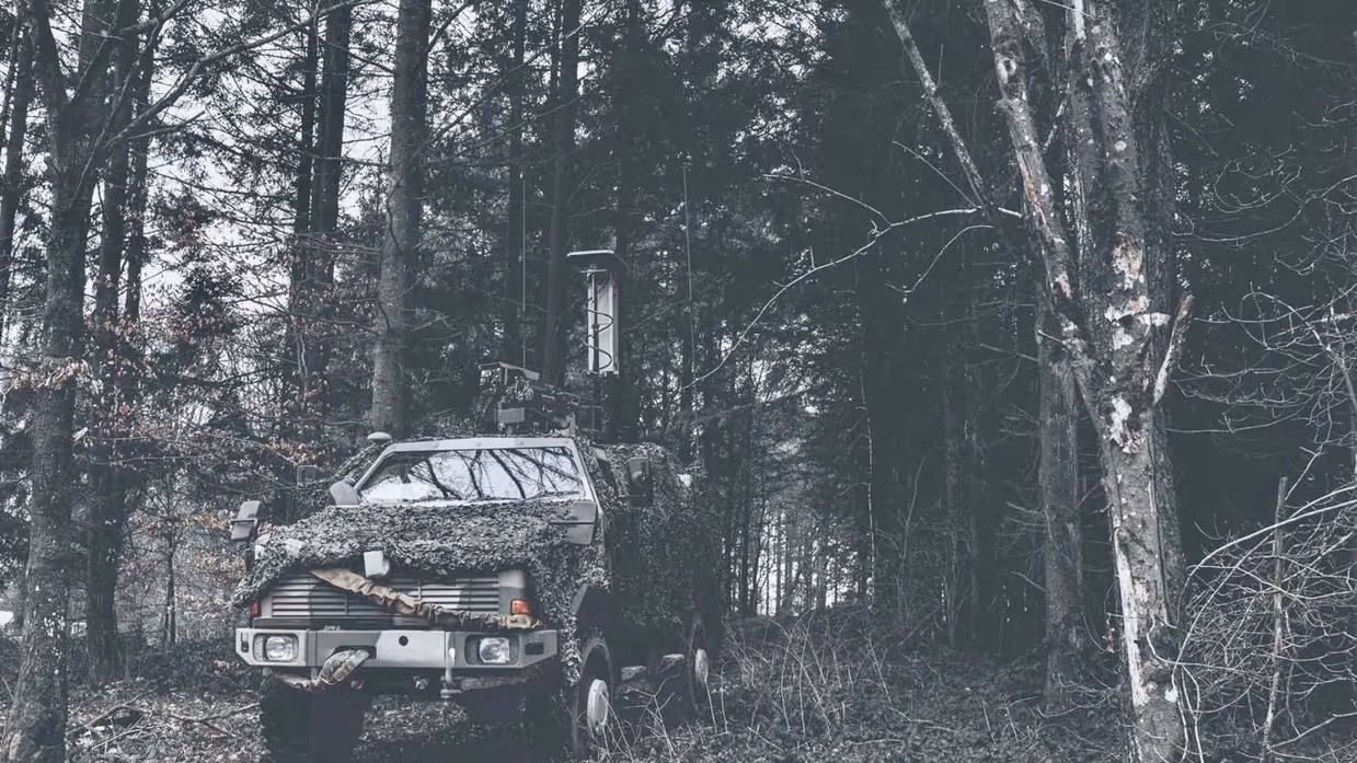 Jeep met camouflage net in het bos.