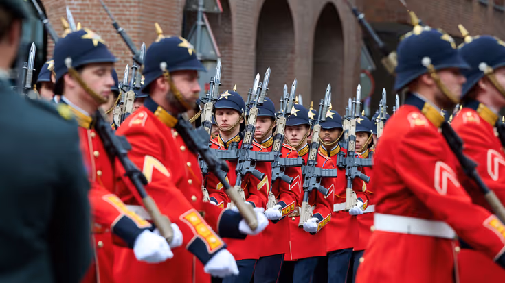 Marcherende militairen in rode jasjes.