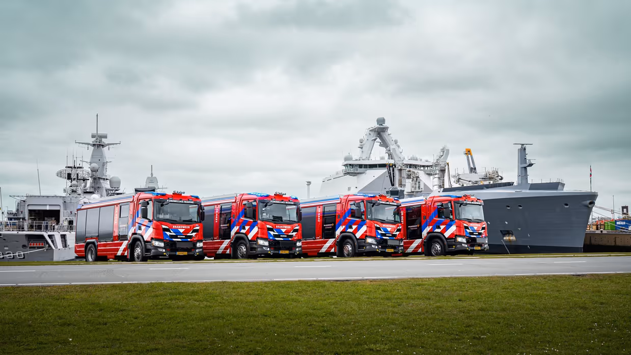 4 brandweerwagens staan naast het bassin van de Nieuwe Haven in Den Helder. Op de achtergrond liggen 2 marineschepen.