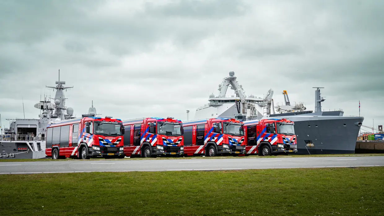 4 brandweerwagens staan naast het bassin van de Nieuwe Haven in Den Helder. Op de achtergrond liggen 2 marineschepen.