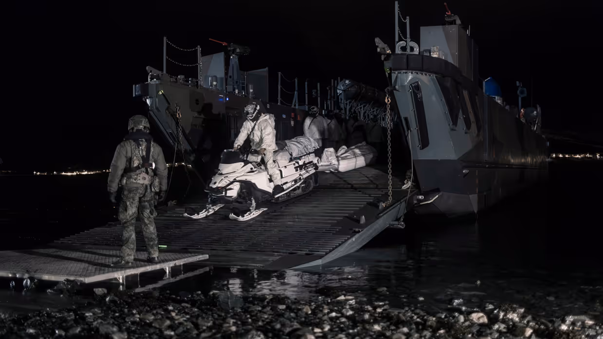  Een marinier in wit pak bestuurt een sneeuwscooter. Hiermee verlaat hij, in het donker, een landingsvaartuig.
