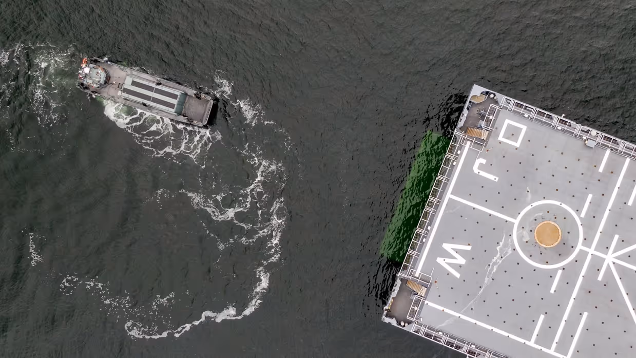 Kleine boot van bovenaf gezien. Dek groot marineschip half in beeld.