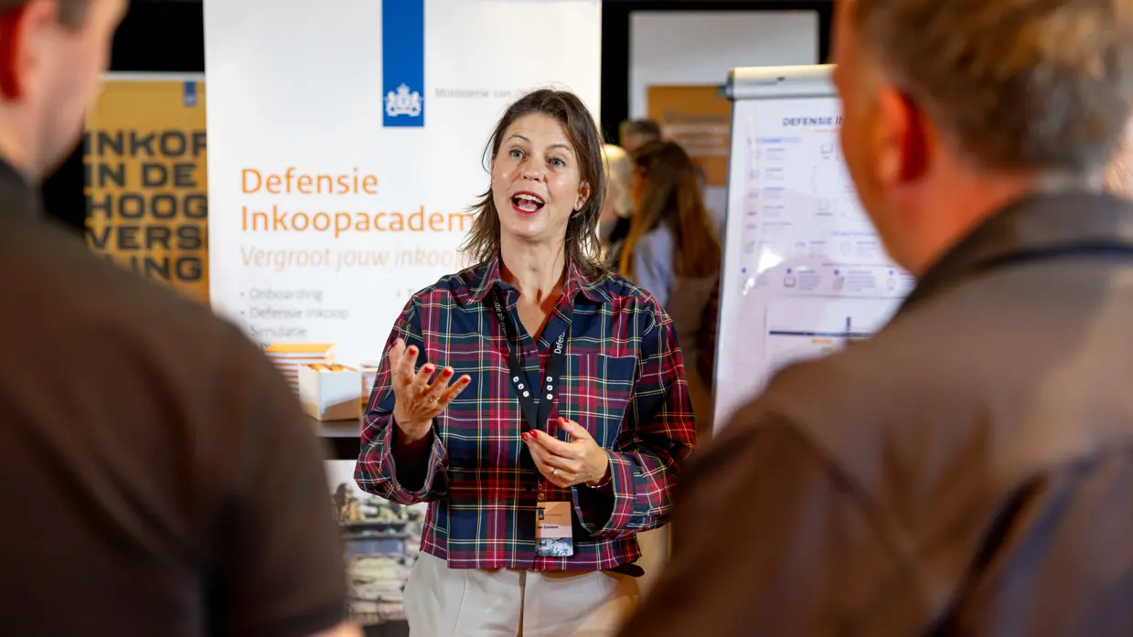 Een vrouw geeft uitleg op de inkoopmarkt waar inkopers van Defensie samenkwamen.