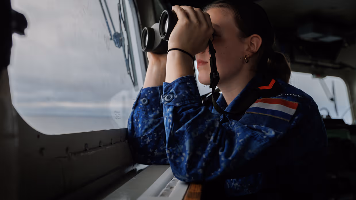 Een vrouwelijke marine-militair kijkt door een verrekijker.