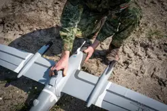 Gehurkte militair werkt aan drone die op de grond ligt.